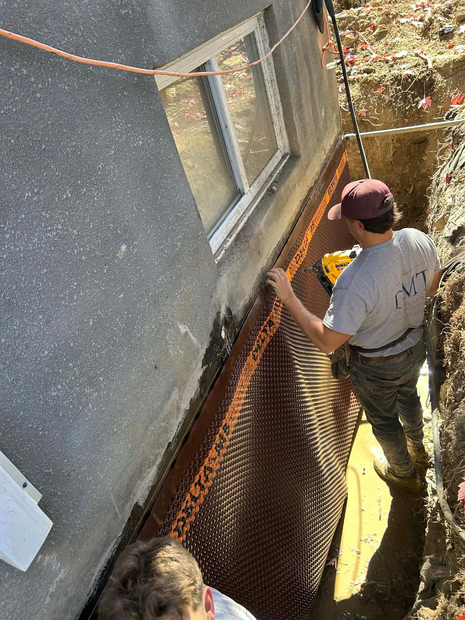Un homme installe un système de drainage sur un mur extérieur. Membrane brune à picots dans la tranchée.