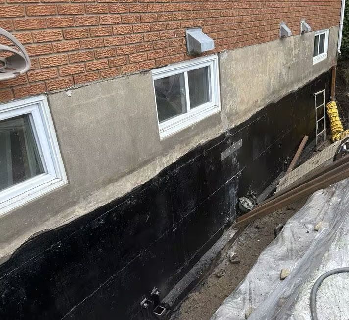 Mur extérieur de la maison avec mastic noir, fenêtres et section de brique lors de la réparation des fondations.