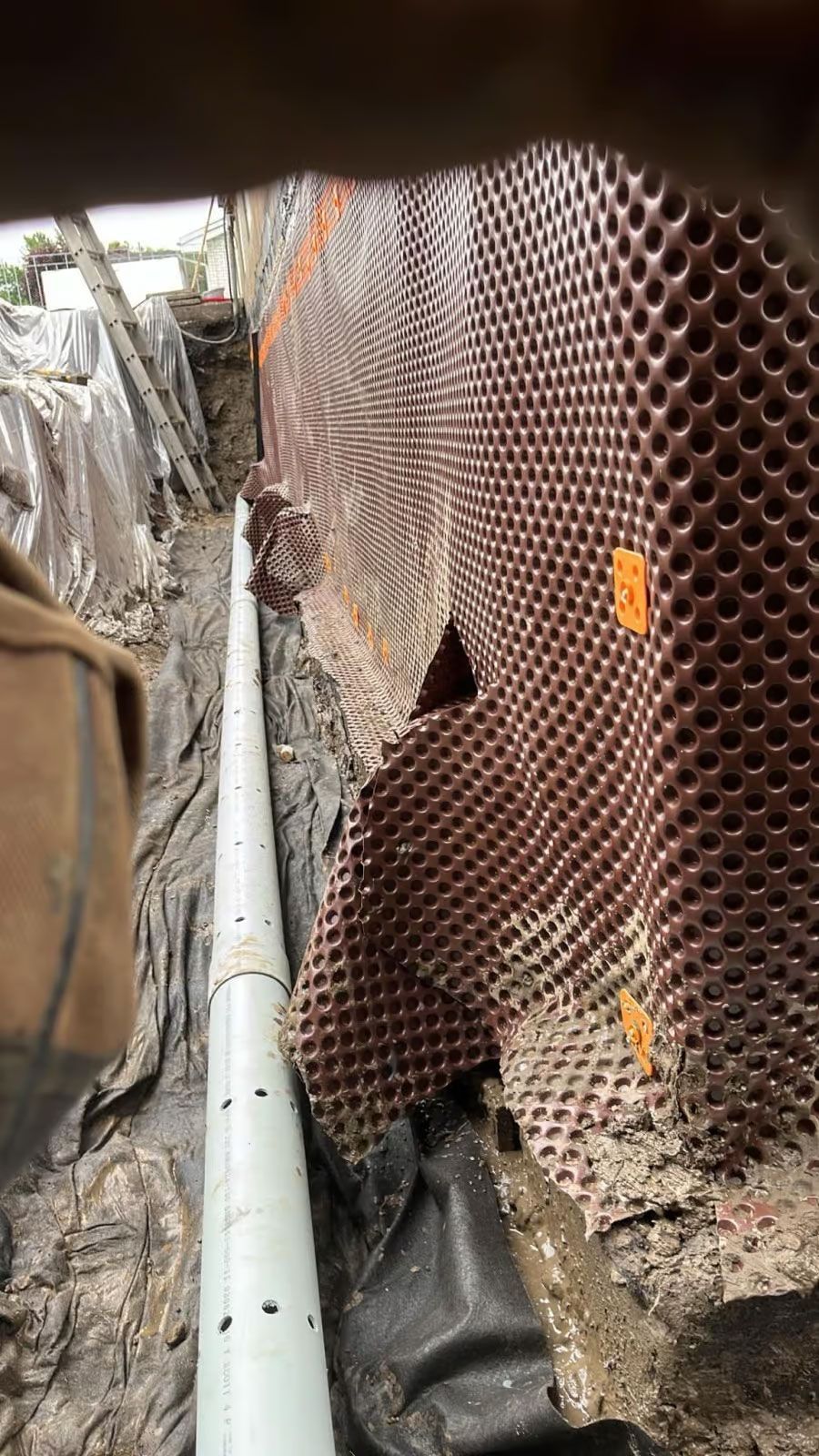 Installation d'un système de drainage avec tuyau perforé et membrane alvéolée dans une tranchée.