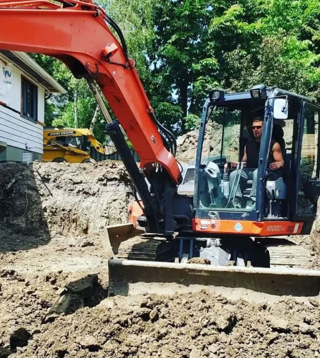 Une excavatrice creuse dans une fosse près d'une maison ; un opérateur se trouve dans la cabine.