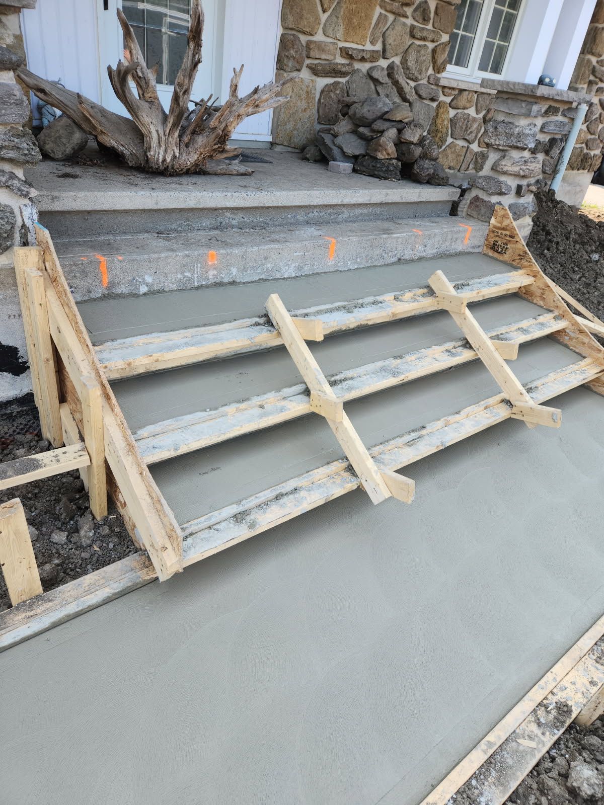 Escaliers en béton en construction devant un bâtiment en pierre, avec des coffrages en bois en place.