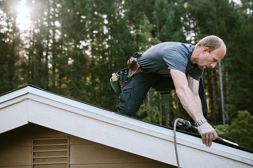 Professional roofer working on house roof with tools in forested area, home improvement.