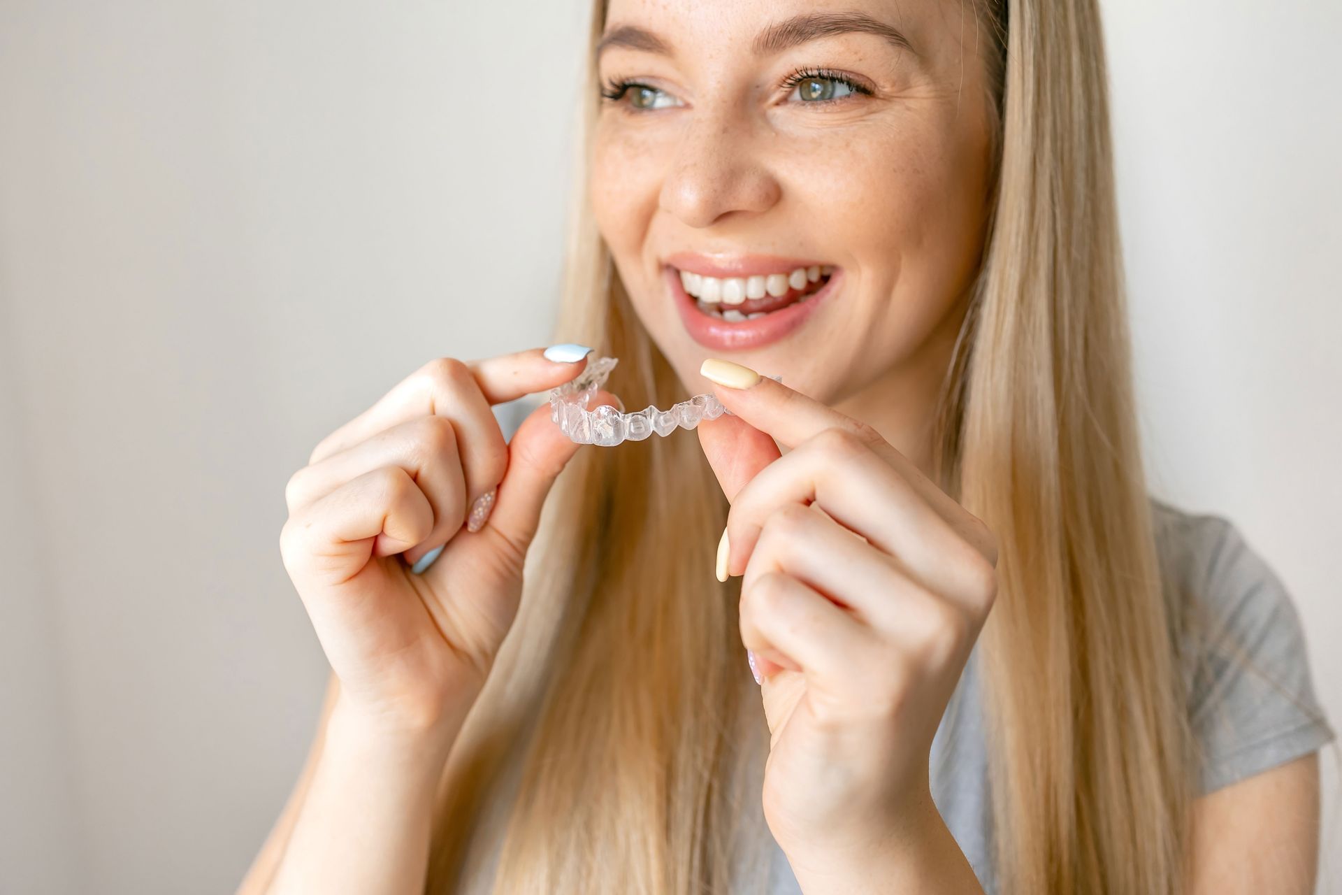A smiling person holding a clear plastic orthodontic aligner tray in their hands against a plain white background.
