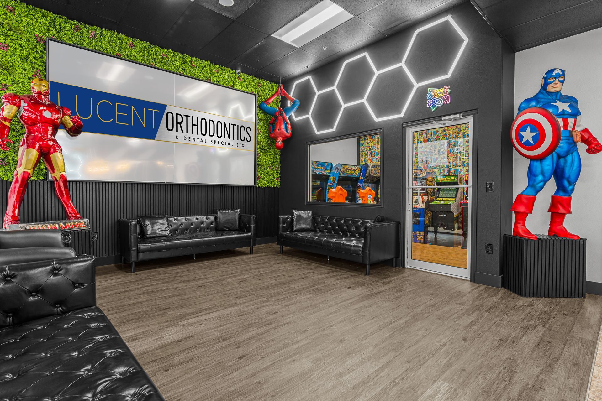Waiting area at Lucent Orthodontics San Antonio featuring superhero statues, leather couches, neon lighting, and faux grass wall.