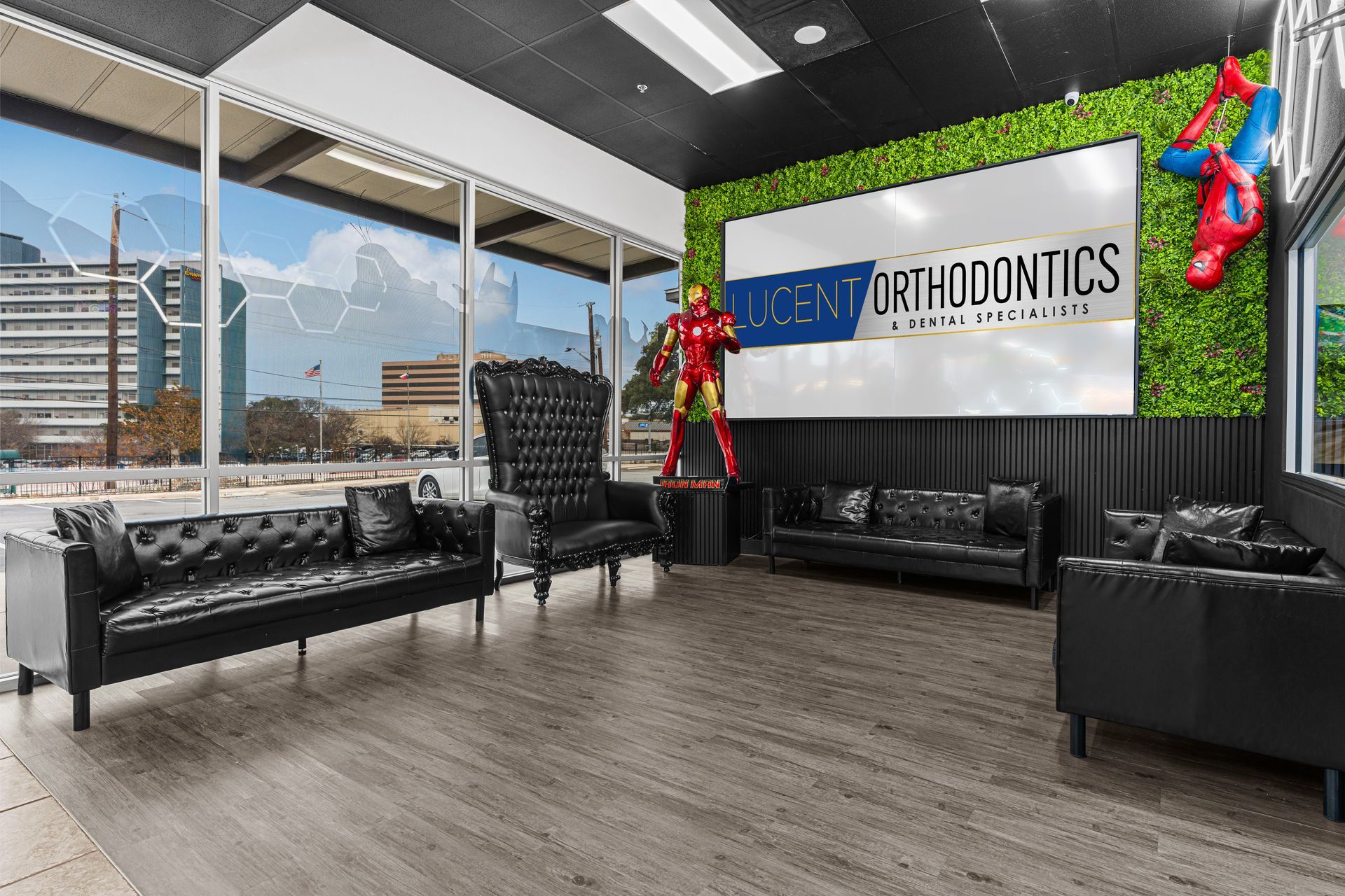 A waiting room with black tufted furniture, a logo for Lucent Orthodontics, and Iron Man and Spider-Man action figures.
