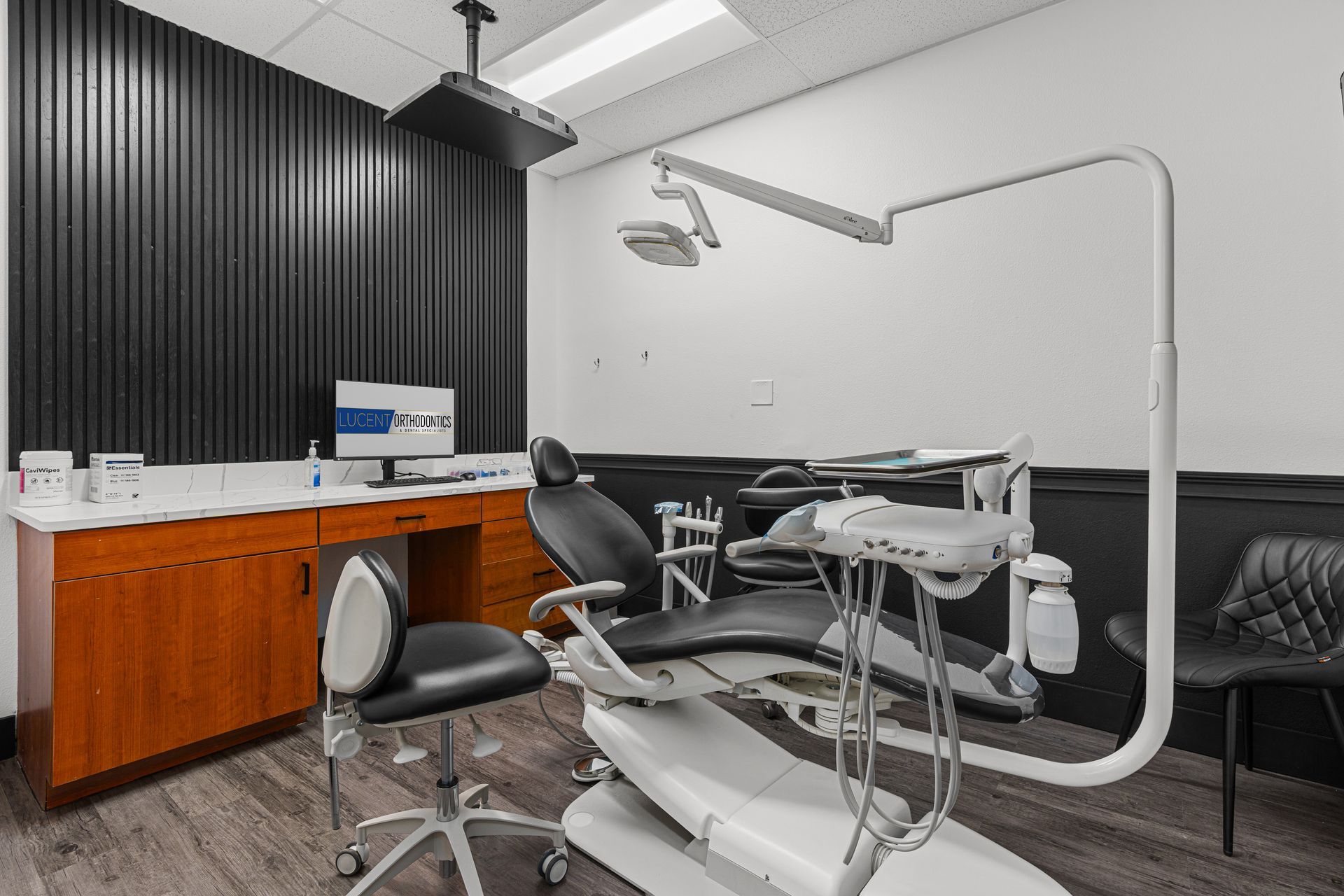 Lucent Orthodontics, San Antonio. A modern dental operatory featuring a reclining patient chair, dental equipment, a computer station, and desk seating.