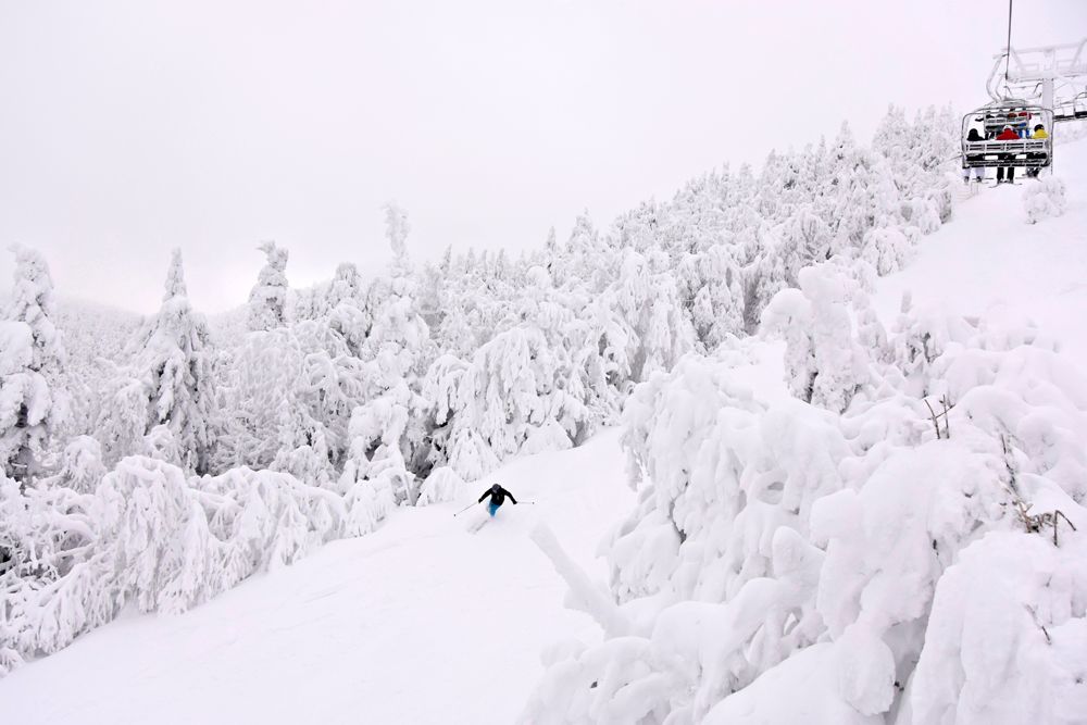 A person is skiing down a snow covered slope next to a ski lift.