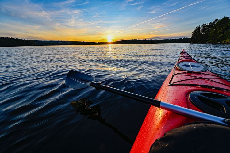 Kayaking on a lake at sunset, red kayak, paddle, sun reflecting on the water.