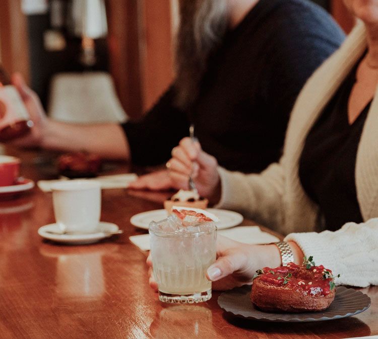 Un groupe de personnes sont assises au comptoir d'un café avec des assiettes de nourriture et de boissons.