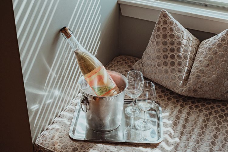 A bottle of wine is in a bucket on a tray next to wine glasses.