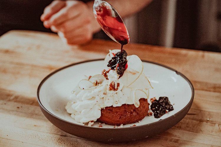 A person is pouring sauce on a dessert on a plate.