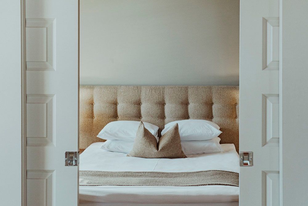 A bed with white sheets and pillows in a bedroom with a door open.