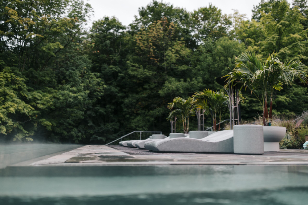 Steaming outdoor pool with a dark triangular deck, white loungers, and palm trees in a lush garden