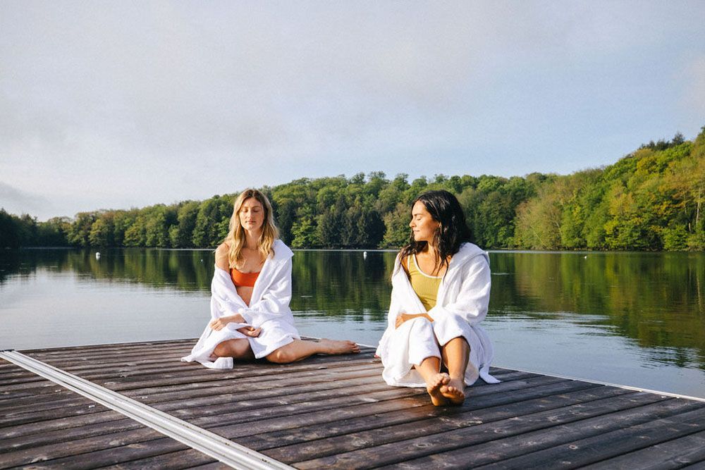 Two women are sitting on a dock next to a lake.