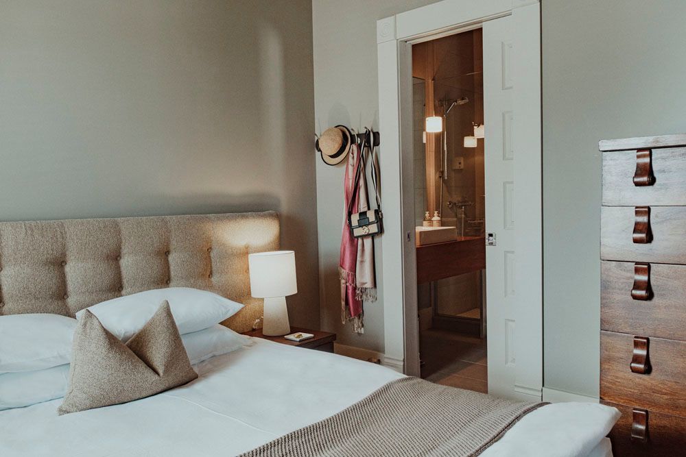 A bedroom with a bed , dresser , lamp and door leading to a bathroom.