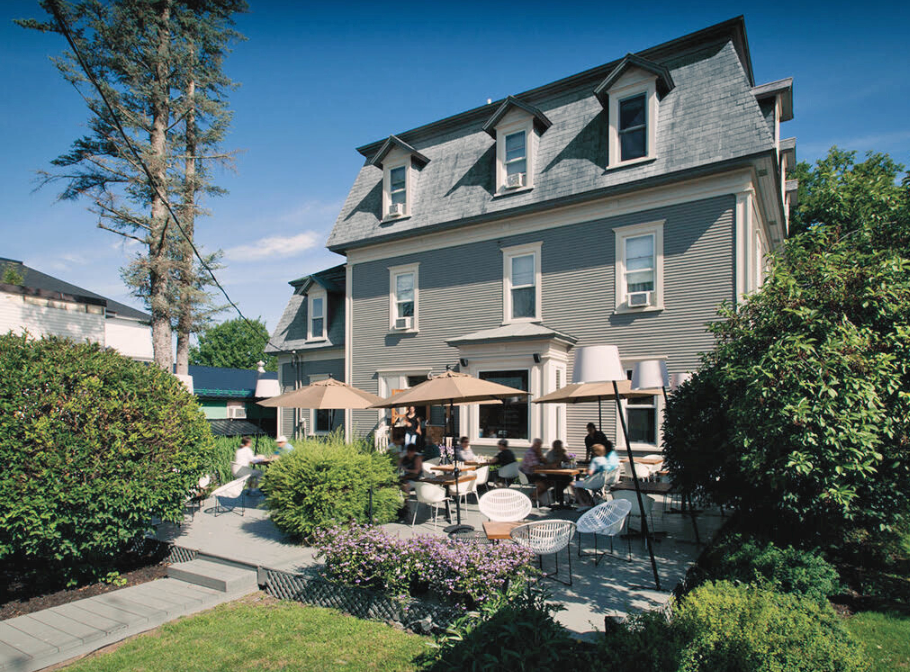 Facade le Le Pleasant Hôtel et Café avec terrasse tables et parasols.