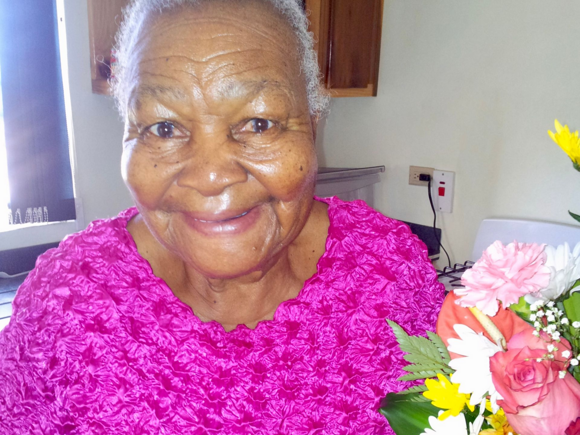 Vera Howlette smiling and holding a bouquet of flowers in Jamaica.