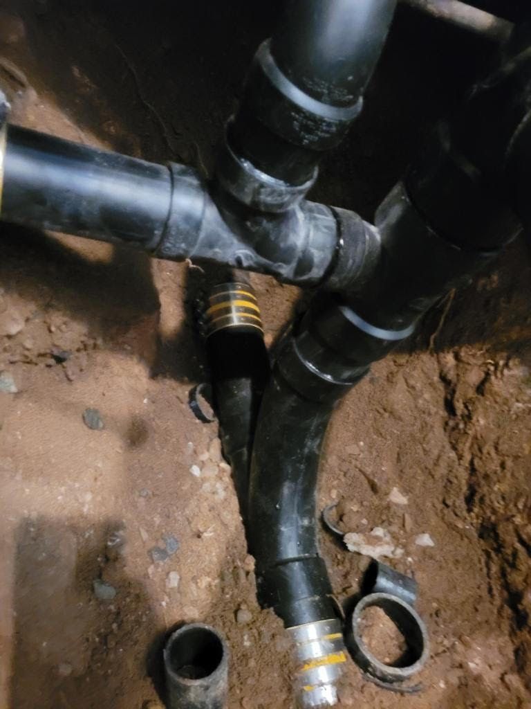 Black plumbing pipes and fittings in a dirt ground, with yellow couplings and a detached pipe section visible.