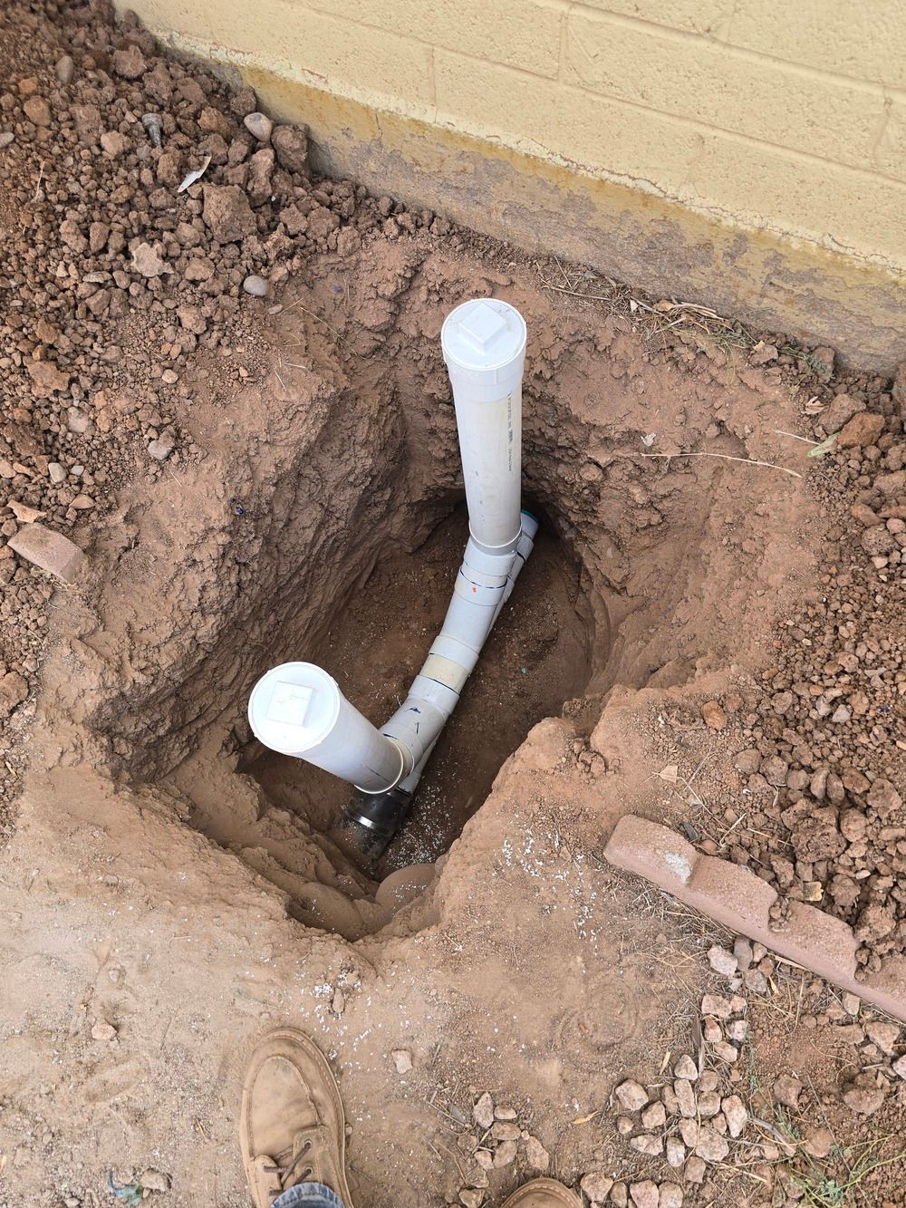 Pipes emerging from a dirt pit against a beige wall; two capped vertical pipes and a bent, capped horizontal one.