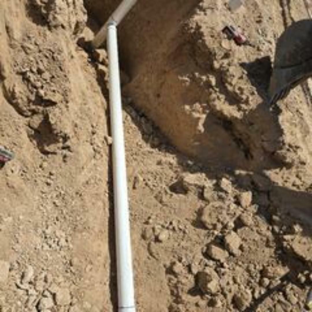 White PVC pipes in a dirt trench, likely for underground utility installation.