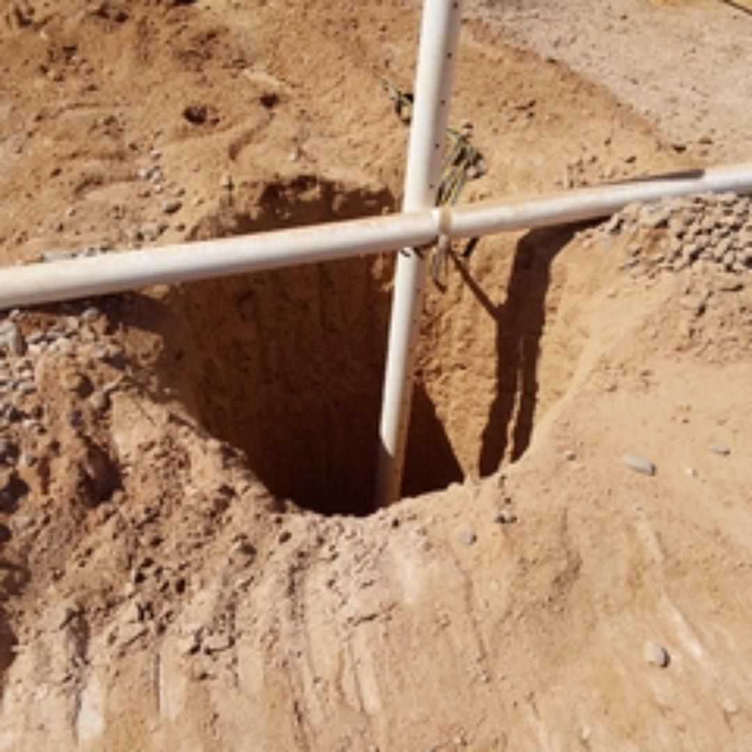 Hole in the ground with white pipes forming a cross, in a dirt setting.