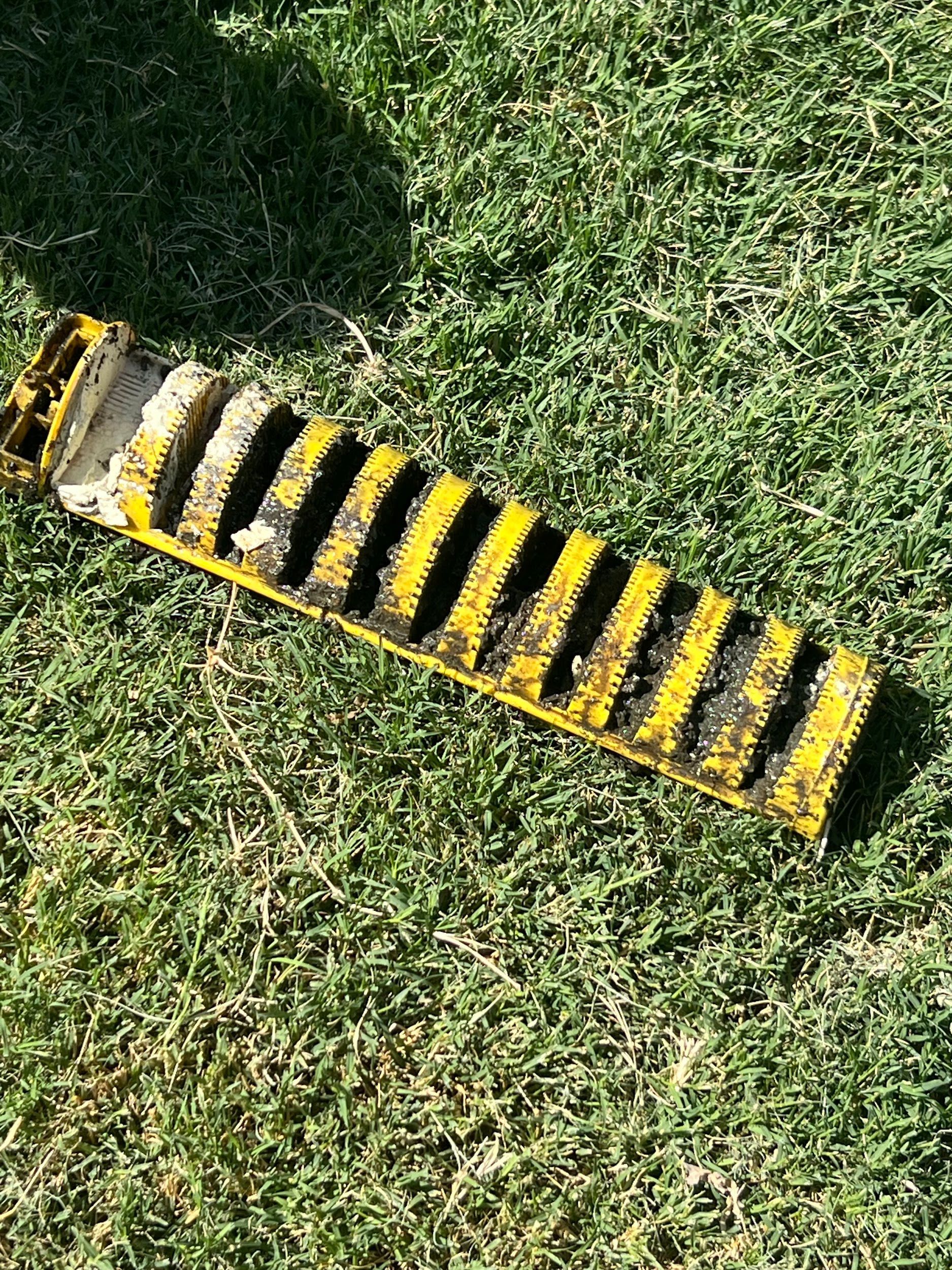 Yellow and black, rectangular drain grate on green grass.