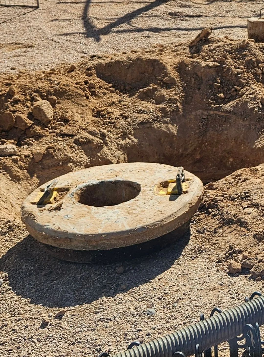 Round concrete object with bolts in a hole dug in dirt, likely for playground equipment.