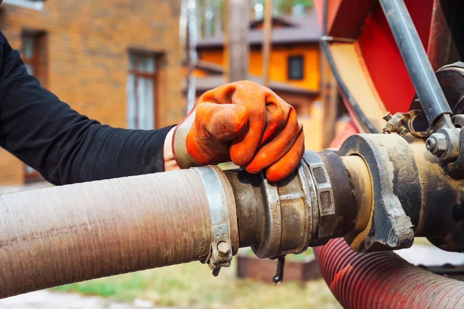 Orange-gloved hand tightening a metal hose coupling on a large industrial pipe outdoors