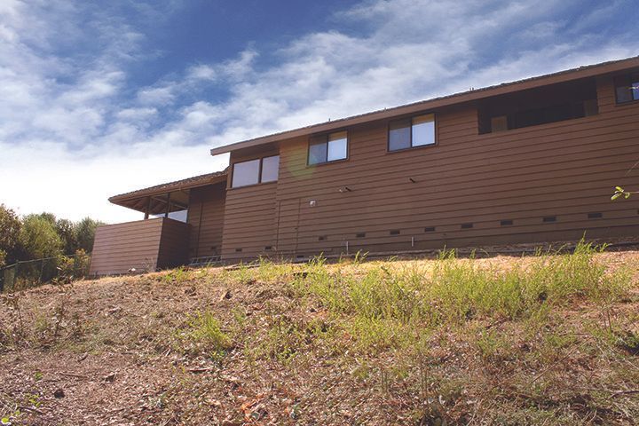 Brown house on a grassy hill, against a partly cloudy sky.