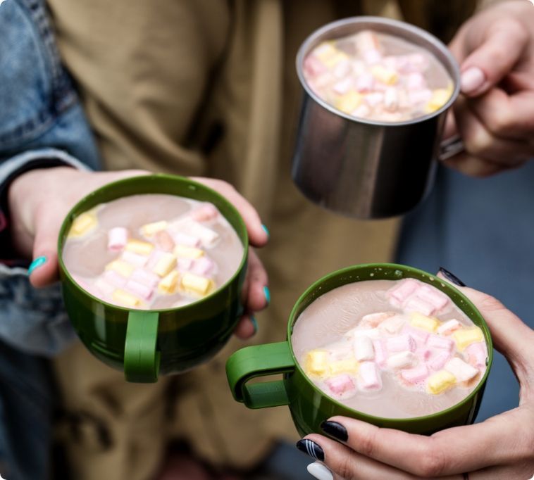 Two people are holding cups of hot chocolate with marshmallows
