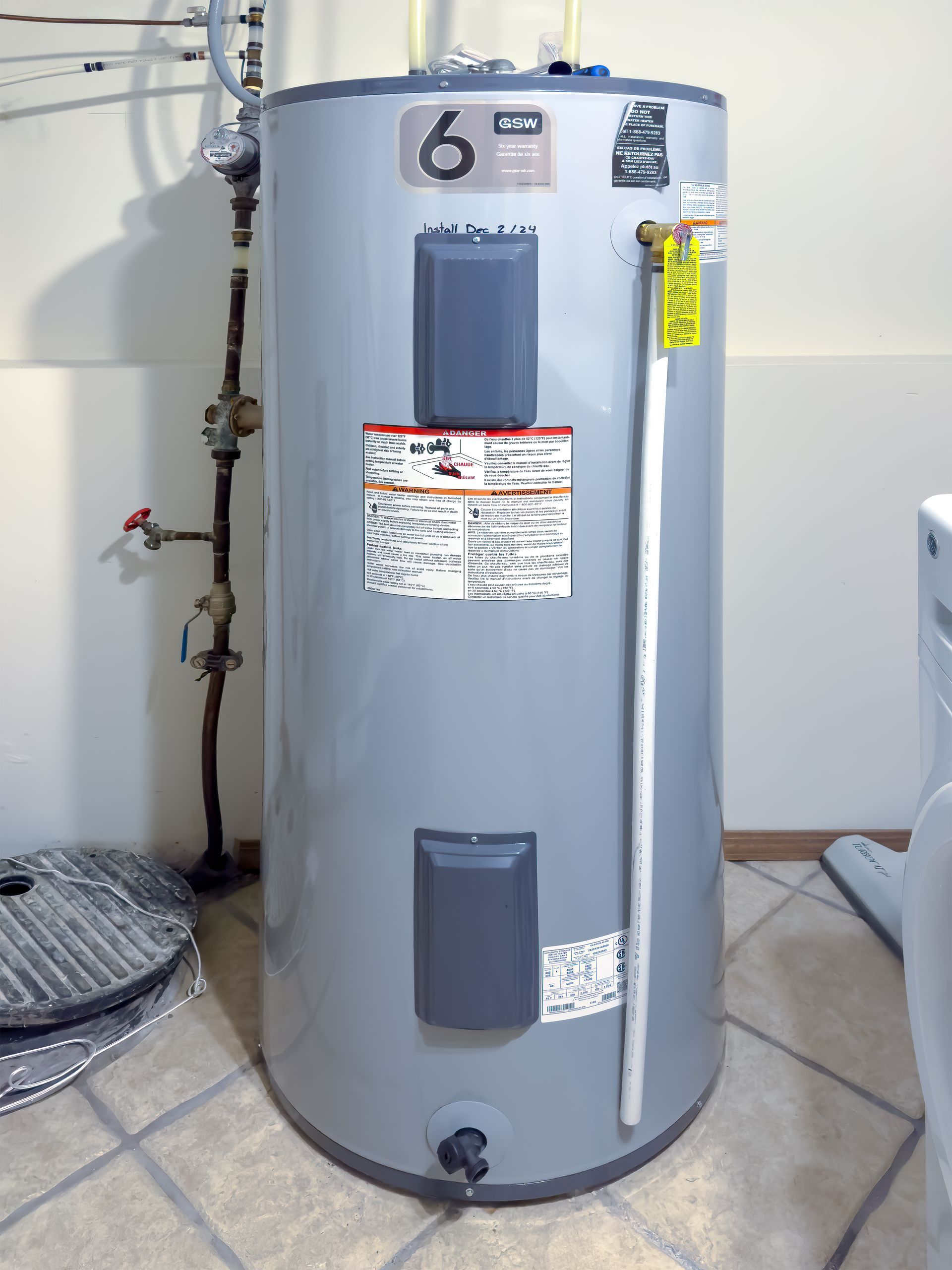 Gray water heater tank with labels and piping in a utility room