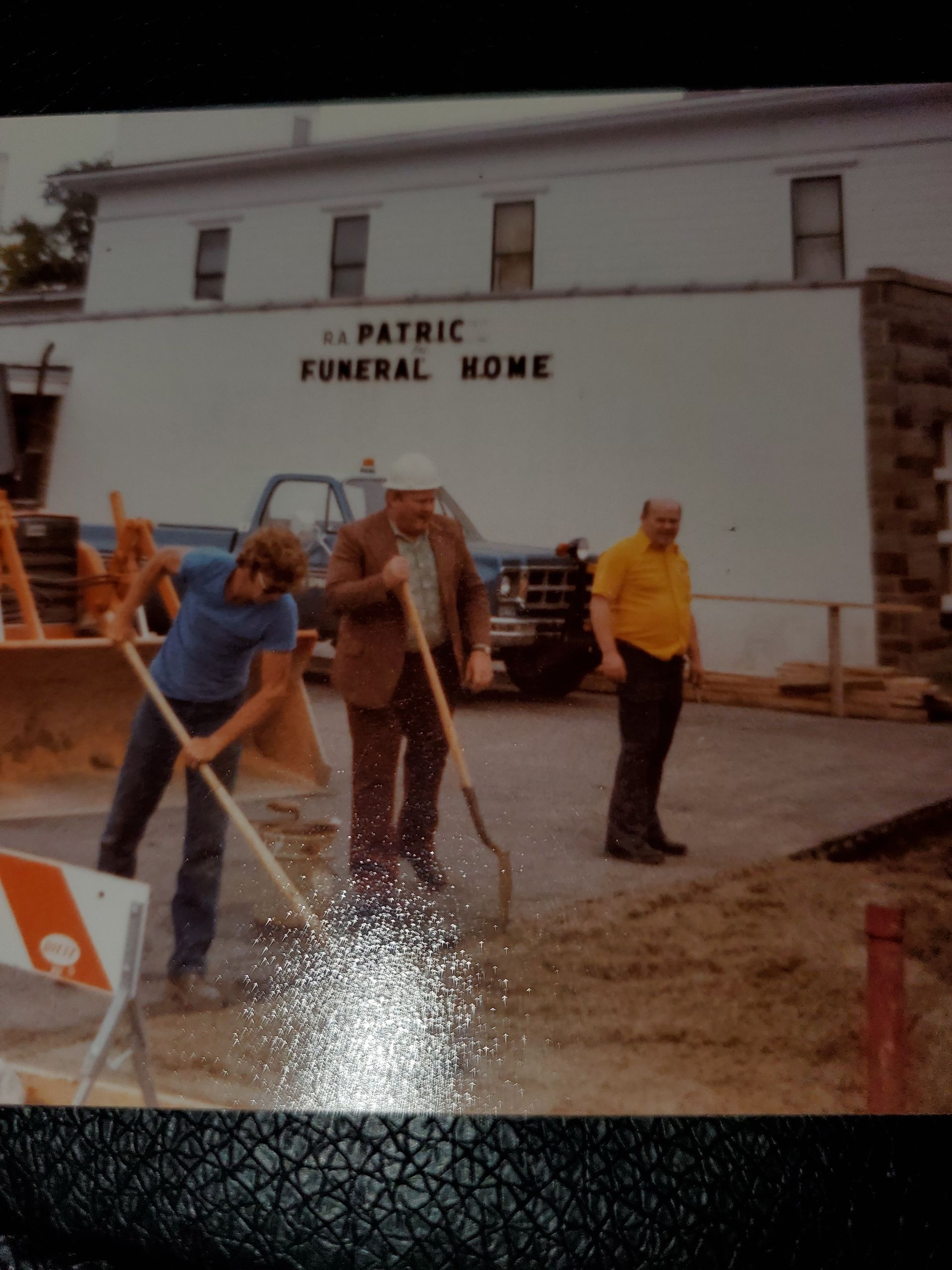 Men working on a construction project outside a funeral home. Two are digging, one is observing.