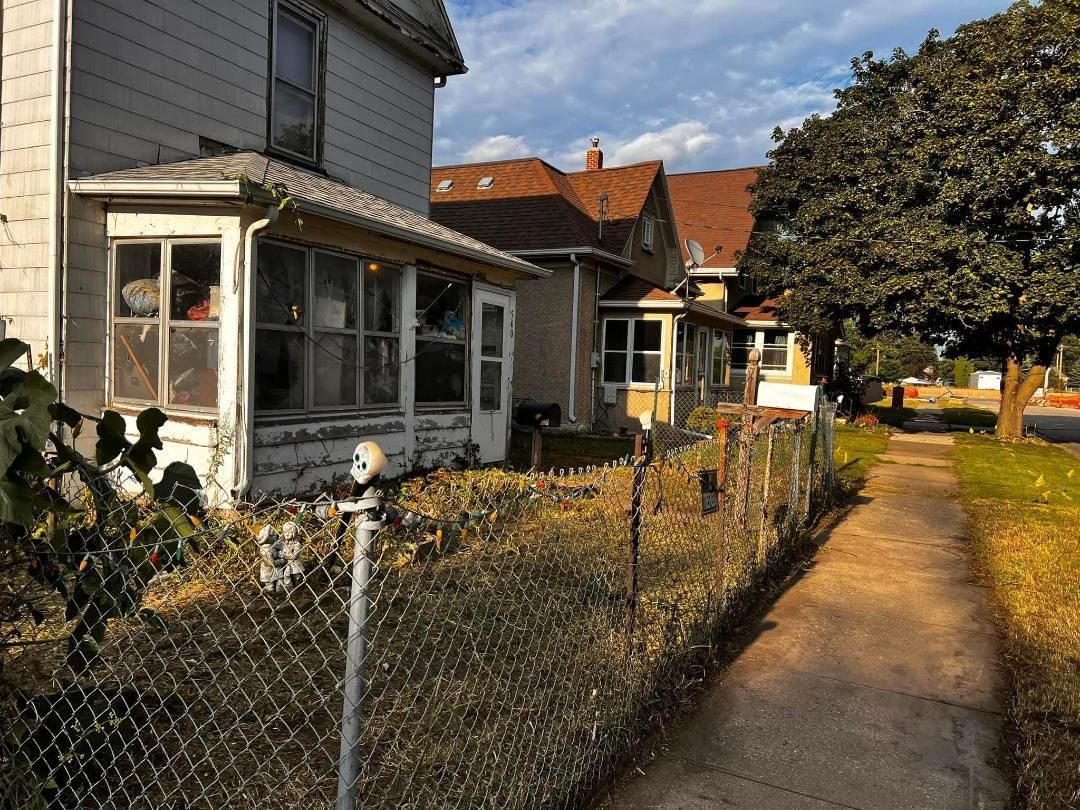 Houses with porches along a sidewalk, with a chain-link fence separating them from the path.