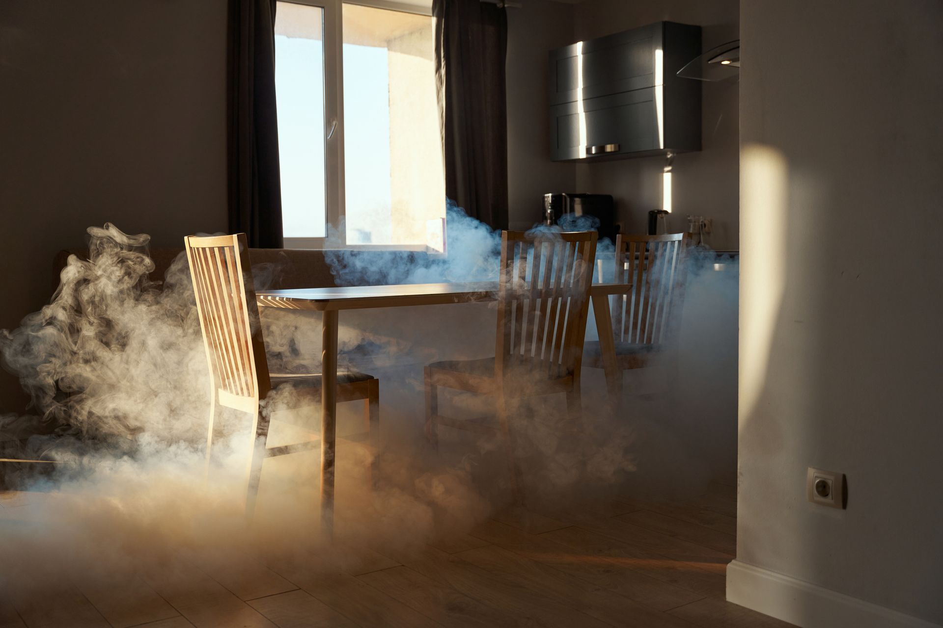 Smoke-filled room with a table, chairs, and sunlight streaming in from a window.