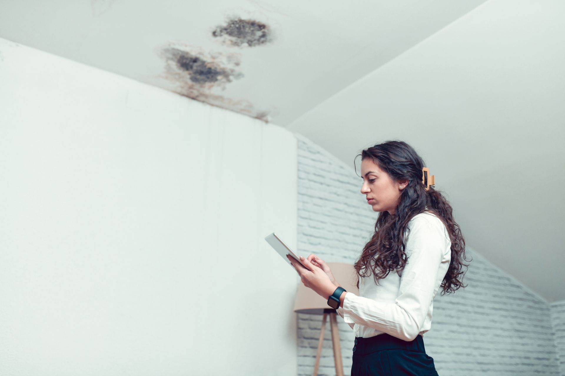 A woman with an iPad in a moldy room highlights the need for home water damage restoration services. A woman with an iPad in a moldy room highlights the need for home water damage restoration services.