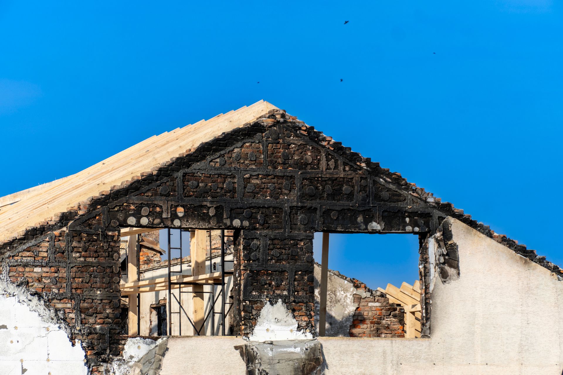 Partially burnt structure of a building in front of the clear blue sky, under the sun.