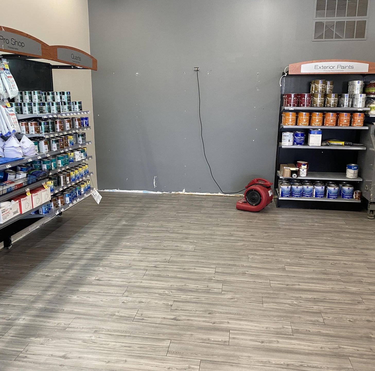 Empty store aisle with gray walls, stocked shelves, and a red fan on the floor.