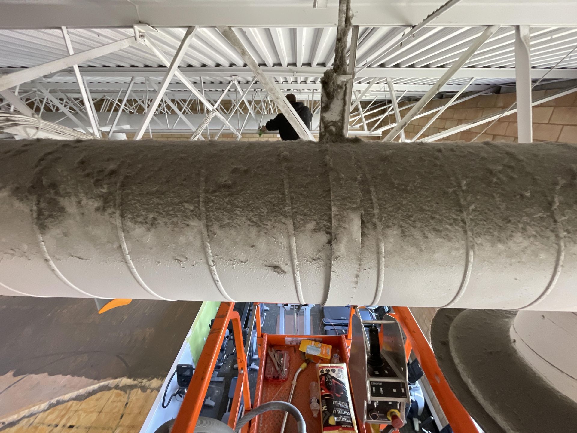 Person working on ductwork, high above the ground; seen from a lift, with industrial setting.