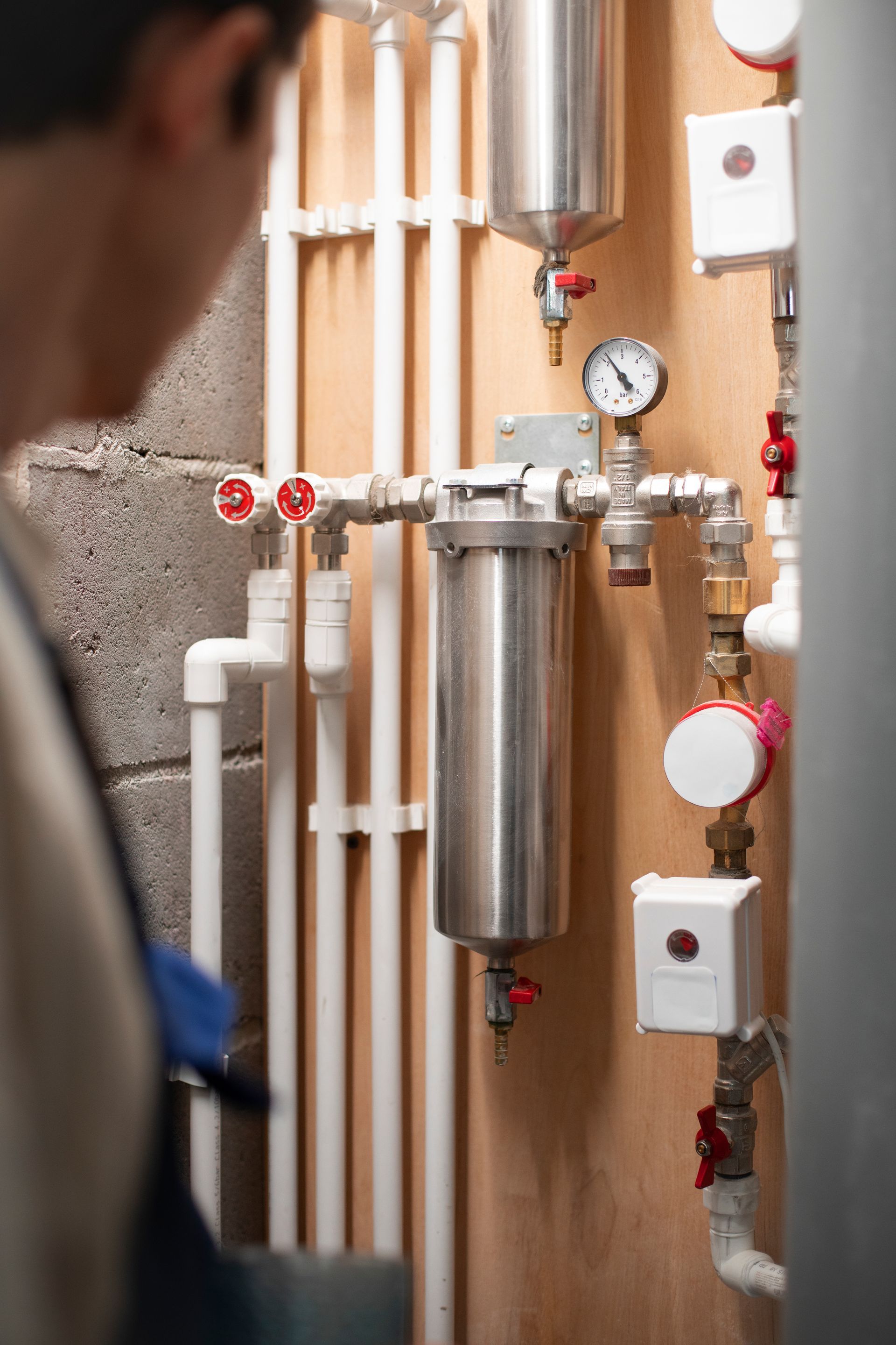A man is standing in front of a wall with pipes and valves.