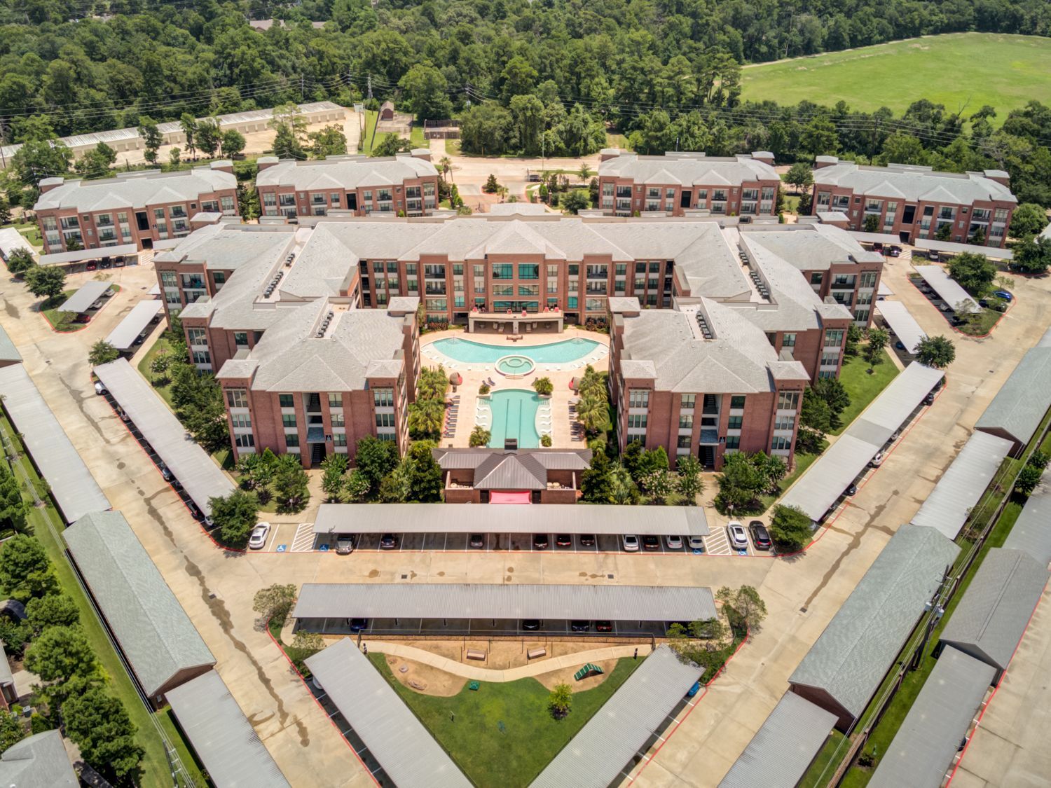 Aerial view of an apartment complex with a pool, brick buildings, and carports.