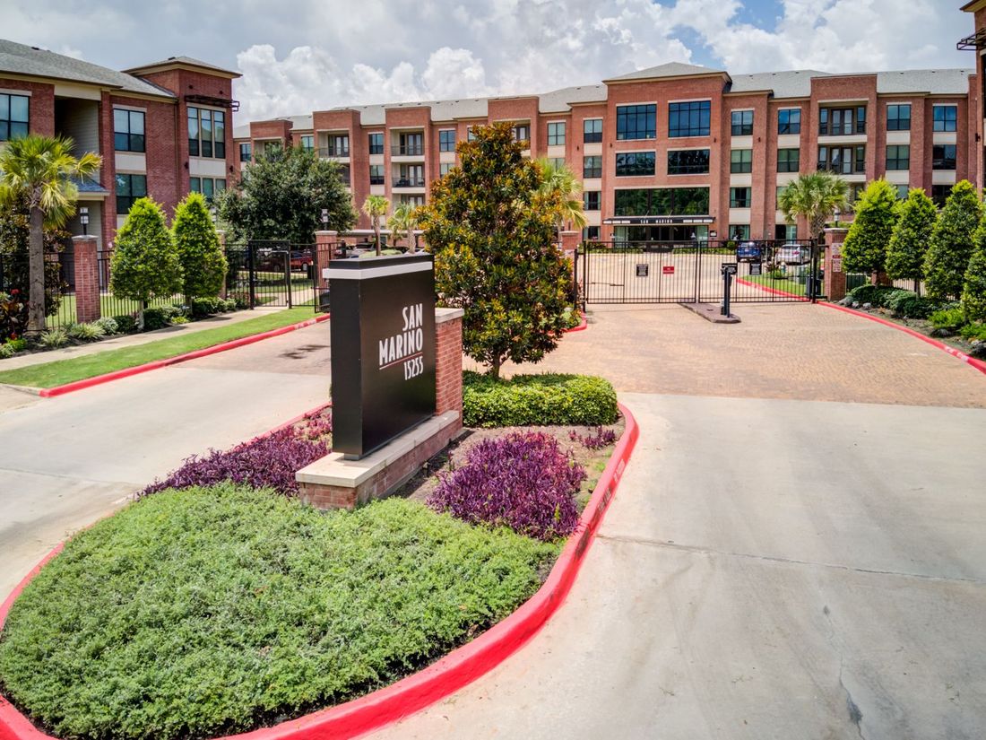 Entrance to San Marino Apartments with sign, gate, brick buildings, and landscaping.