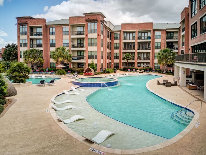 Apartment complex pool with lounge chairs and fountain, surrounded by brick buildings.