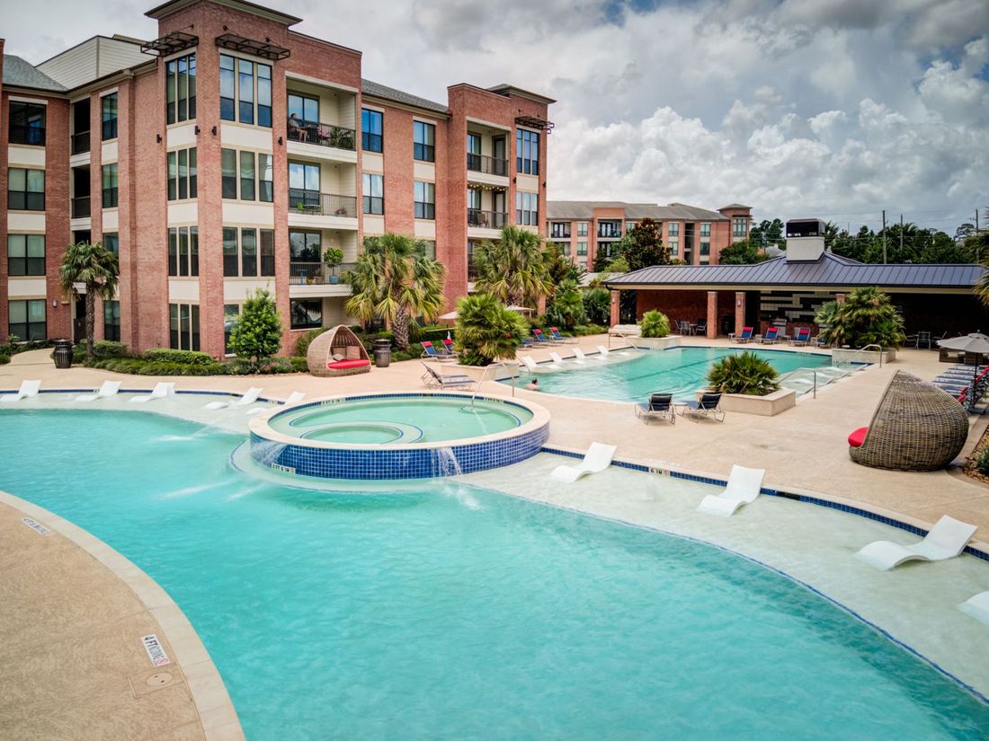 Apartment complex with a large pool area including a lazy river, spa, and lounge chairs.