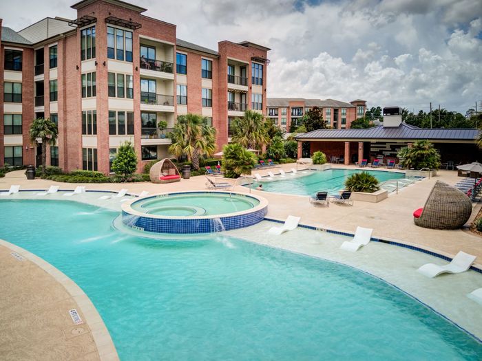 Apartment complex with a large pool area including a lazy river, spa, and lounge chairs.