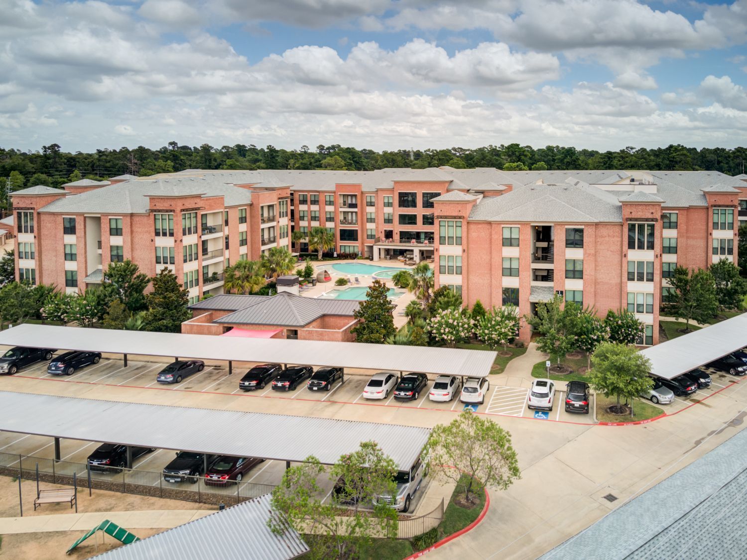 Apartment complex with covered parking, pool, and brick exterior under a cloudy sky.