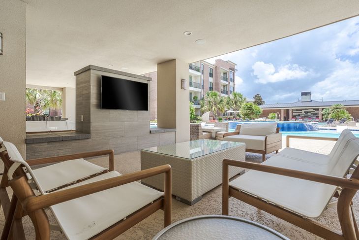 Outdoor lounge area with white furniture, TV, and a pool view.