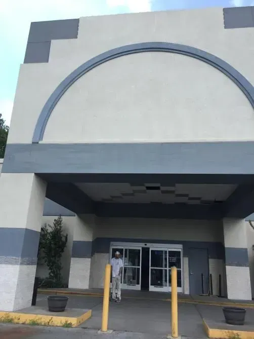 Entrance to a building with automatic doors; a person stands in the doorway. The building is white and gray, with an arched design.
