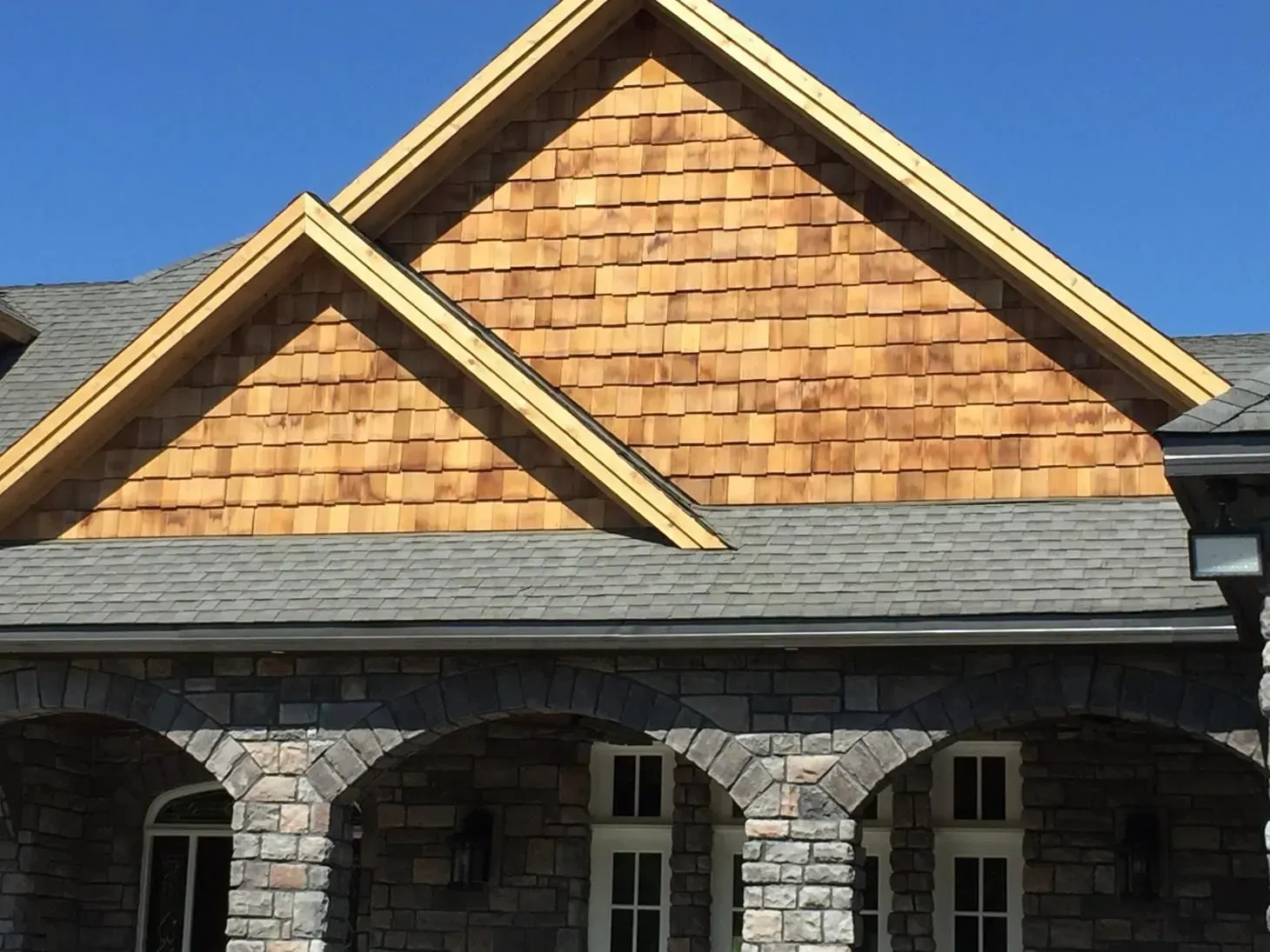 Stone building with arched windows and cedar shingle gables against a clear blue sky.