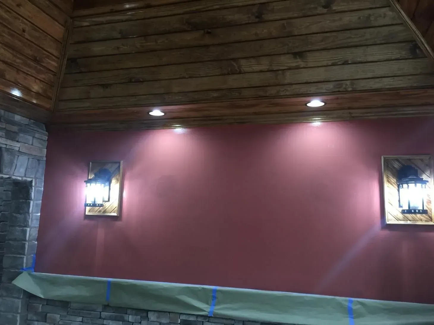 Interior with burgundy wall, wood ceiling, stone fireplace. Two wall sconces and recessed lights illuminate the space.