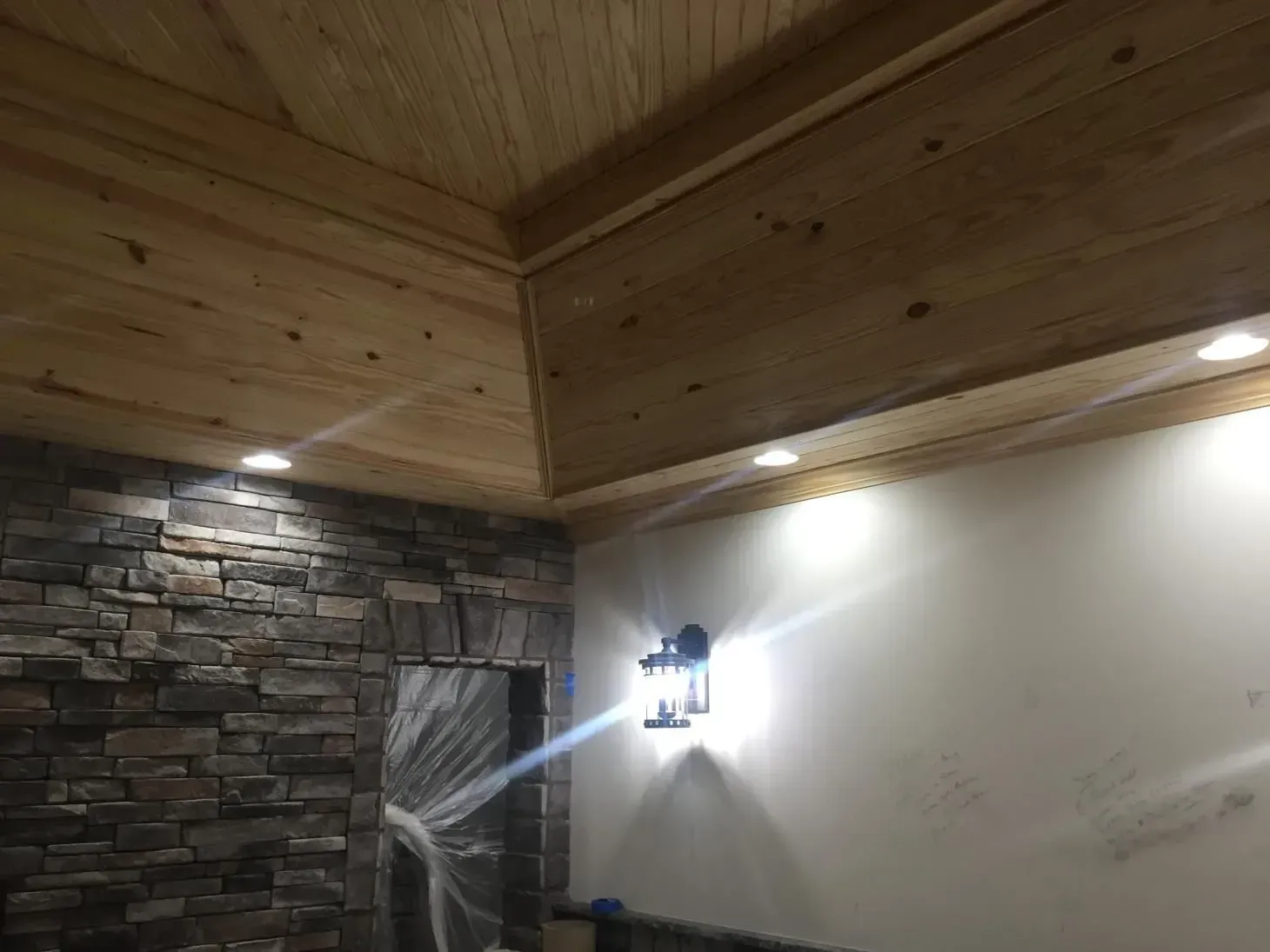 Interior room with a stone wall, wooden ceiling, and a sconce. Bright recessed lights illuminate the space.